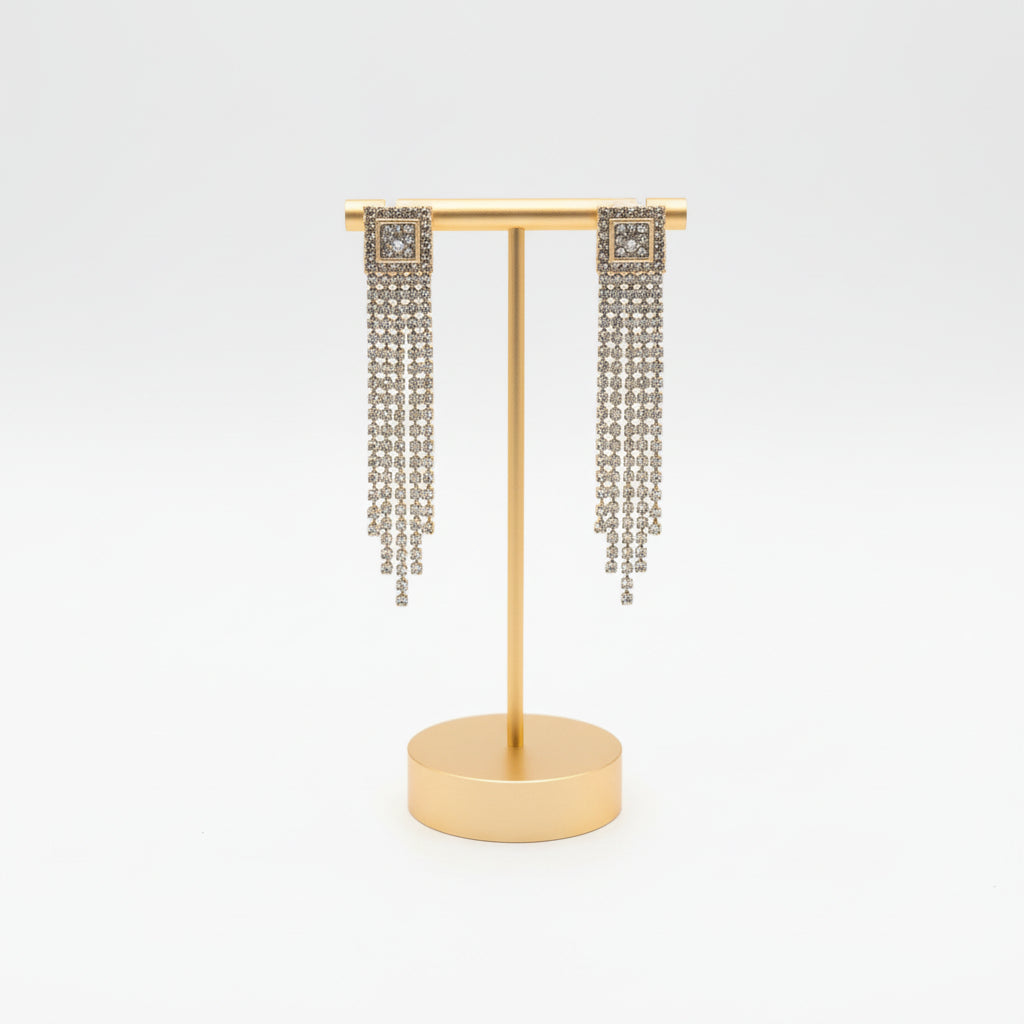 A pair of Square Rhinestone Waterfall Dangle earrings from Cheveux Extensions by Mar rests in a gray velvet jewelry box beside a gold earring adorned with round pearl accents.