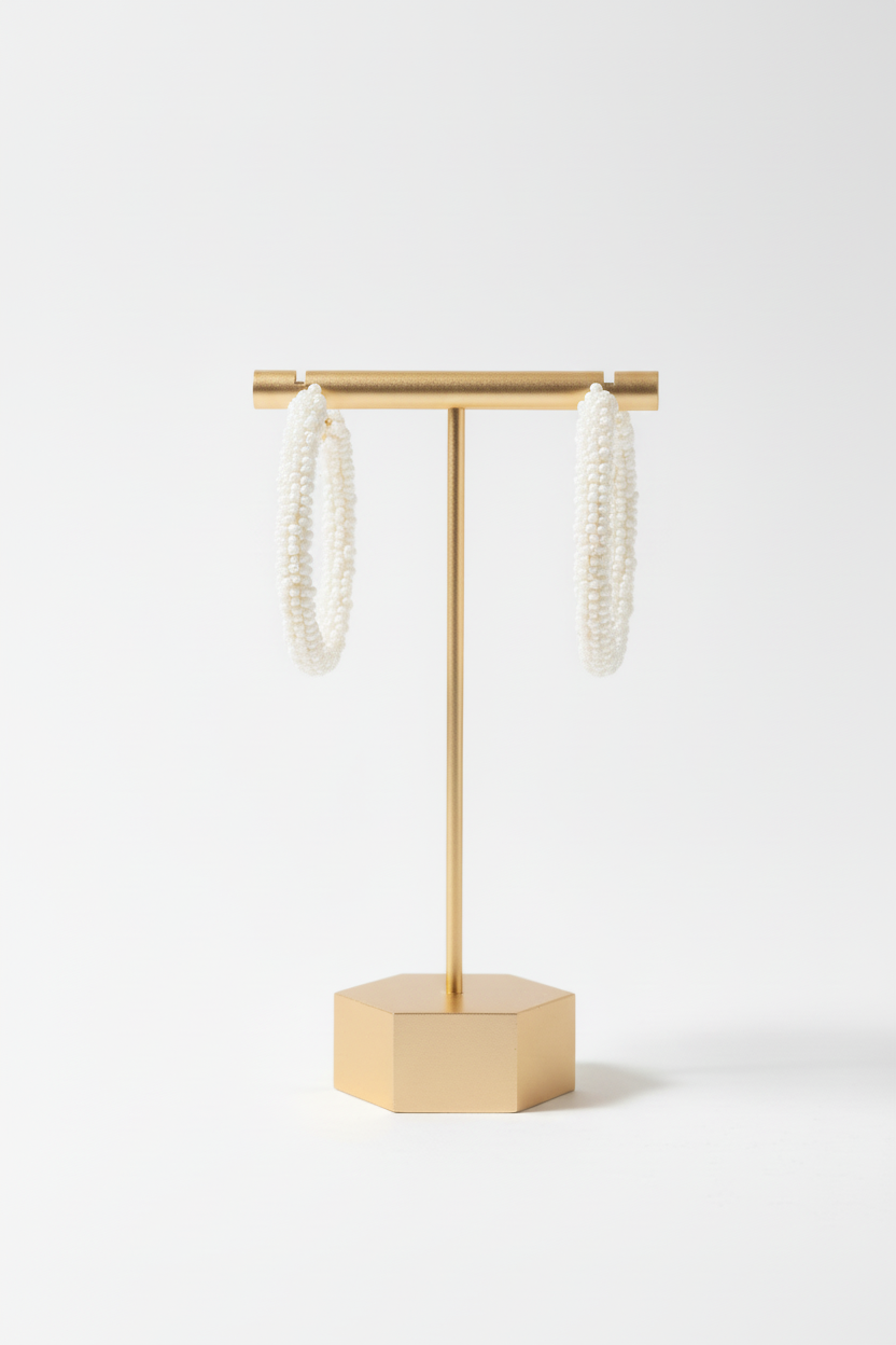 A hand holds a display card featuring Cheveux Extensions by Mar's Beaded Stars with pearl small Hoops, adorned with clusters of white and pink beads, set against a white wall background.