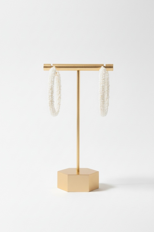 A hand holds a display card featuring Cheveux Extensions by Mar's Beaded Stars with pearl small Hoops, adorned with clusters of white and pink beads, set against a white wall background.