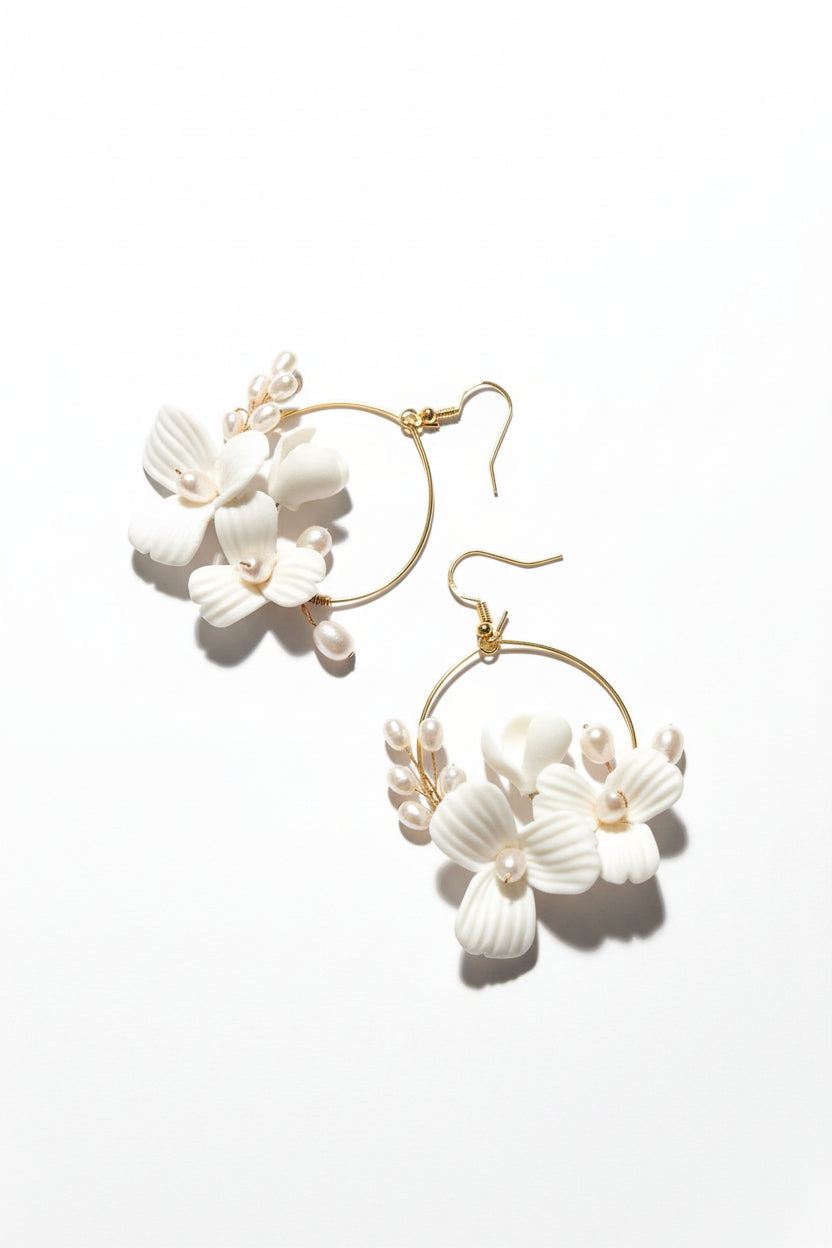 Gold hoop earrings with white floral designs on a beige background