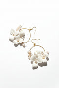 Gold hoop earrings with white floral designs on a beige background
