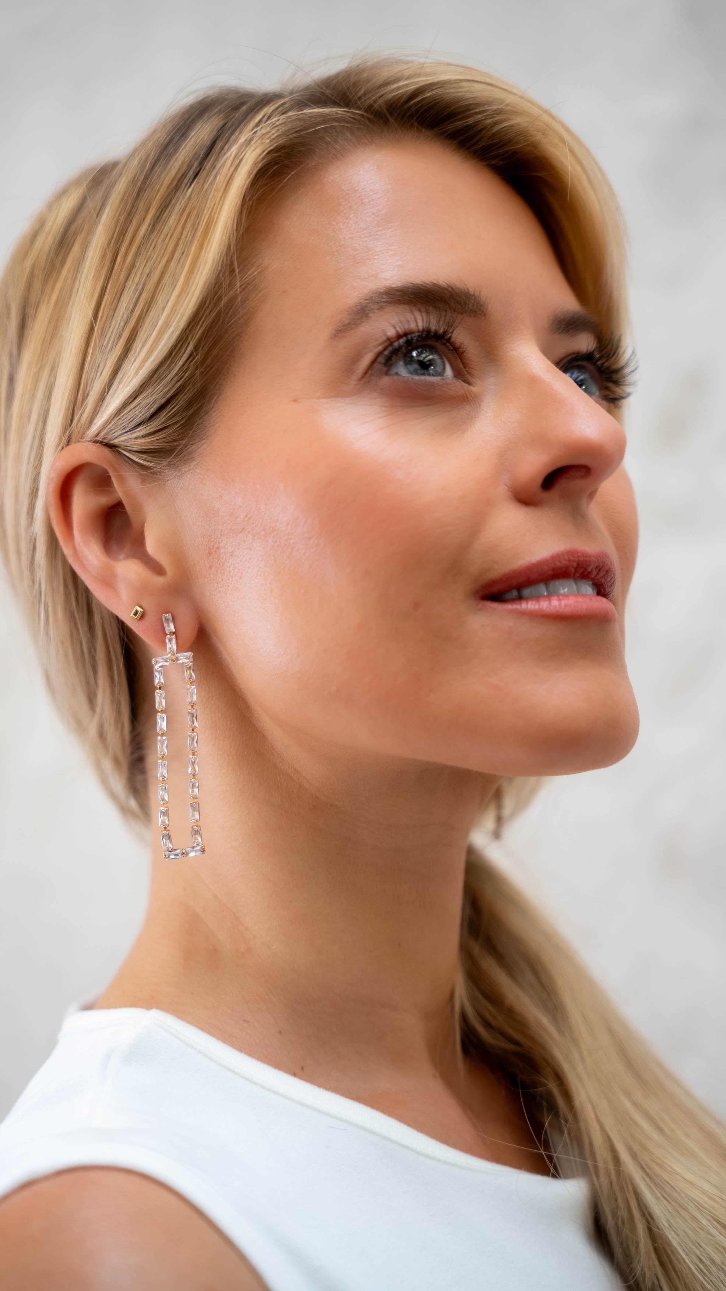 Woman wearing long, dangling earrings against a neutral background
