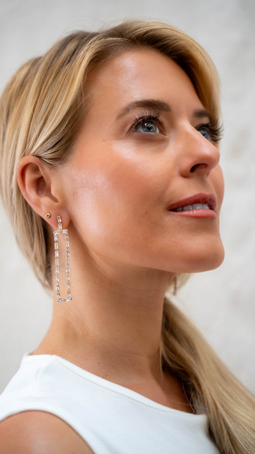Woman wearing long, dangling earrings against a neutral background