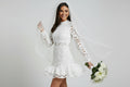 Zarina elegant bridal dress Woman in a white lace wedding dress holding a bouquet against a plain background