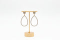 A pair of gold teardrop stud earrings with rhinestone embellishments, displayed on a gold stand